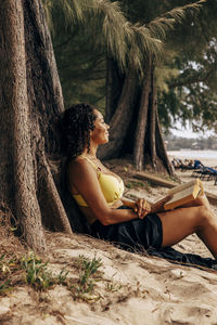 Side view of mature woman reclining on tree trunk with book at beach