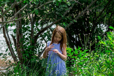 Young girl surrounded by green grass playing with a flower