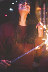 Young woman looking at illuminated camera at night