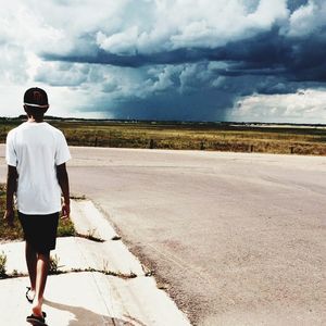 Rear view of man walking on road against cloudy sky