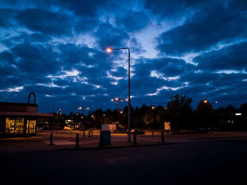 Illuminated lamp post on road against cloudy sky