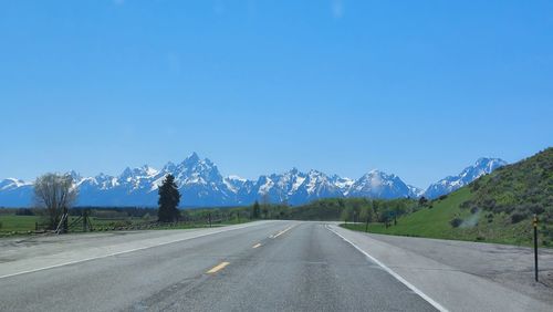 Empty road leading towards mountains against blue sky