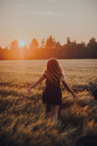 Rear view of woman walking on field against sky during sunset