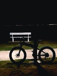 Bicycle parked by railing at lake against sky at night