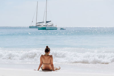 Young woman on tropical sandy beach, light and airy, waves, sailboats.
