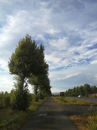 Empty road along trees and landscape against sky