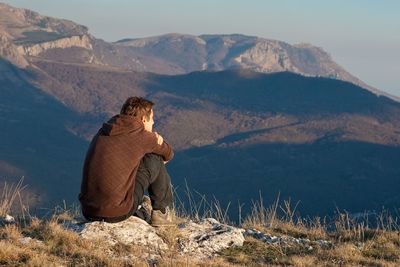 Man sitting on mountain against sky