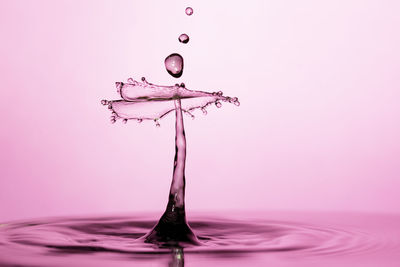 Close-up of water splashing against pink background