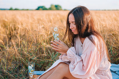 Midsection of woman holding glass while sitting on field