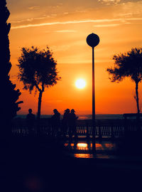 Silhouette people on street against orange sky