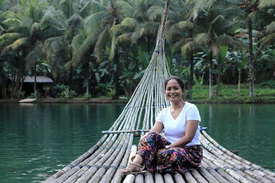 Full length of woman sitting on lake against trees