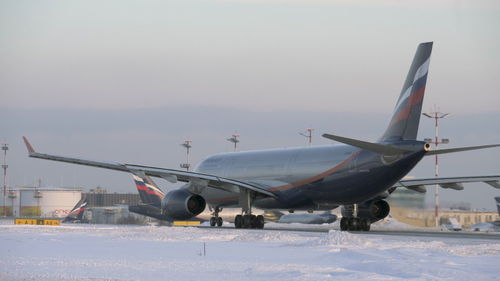 Airplane flying over snowy field against sky during winter