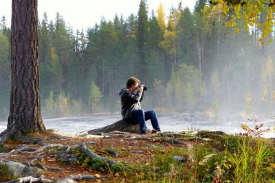 Full length side view of man photographing while sitting at river shore