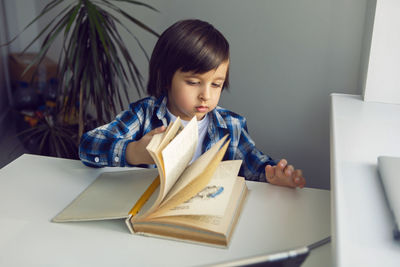 Boy child sits at a desk and learns with a tablet notebook and book