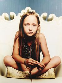 Portrait of a young woman sitting against wall