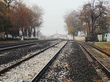 Empty railroad tracks by trees against clear sky during foggy weather