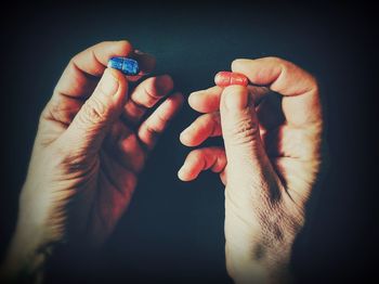 Cropped hands holding red and blue pills against black background