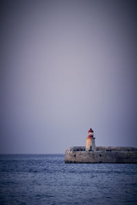 Lighthouse by sea against clear sky