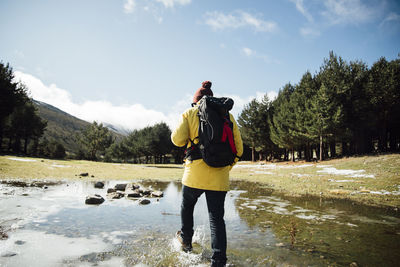 Young man with yellow jacket and backpack next to pond in the mountain