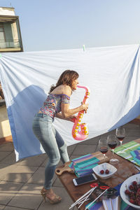 Side view of woman playing toy saxophone while standing on terrace