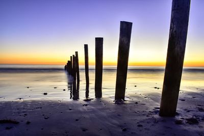 Wooden posts on beach against sky during sunset