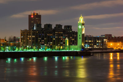 Illuminated buildings by river against sky in city at night