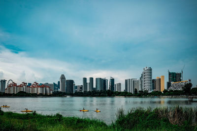 People kayaking in river by buildings against sky