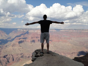 Rear view of man standing on rock against sky