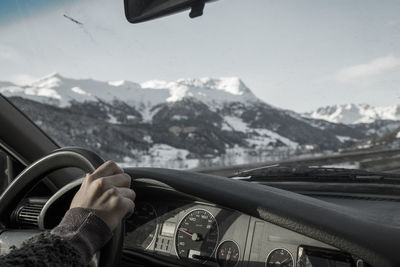 Cropped hand driving car against snowcapped mountains