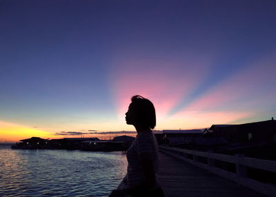 Silhouette woman standing on shore against sky during sunset