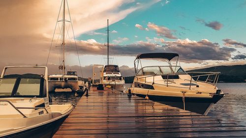 Sailboats moored at harbor against sky during sunset