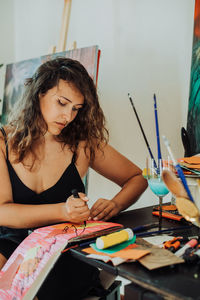 Woman painter focused on work sitting at table in her studio, close up