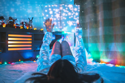 Rear view of woman holding book with illuminated lights on bed at home