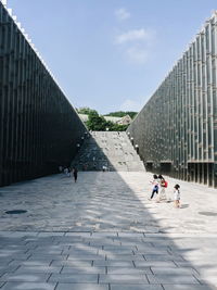 People walking on footpath by building against sky