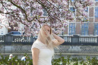 Beautiful young woman with long hair looking at blooming tree with pink magnolia