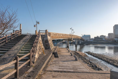 Bridge over river by buildings against clear sky