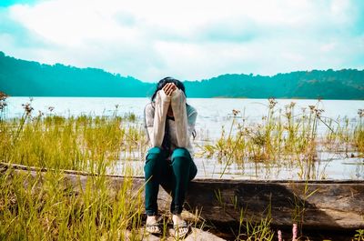 Young woman sitting by plants against sky