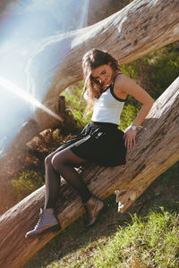 Full length of young woman sitting on fallen tree