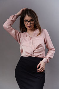 Portrait of young woman standing against gray background