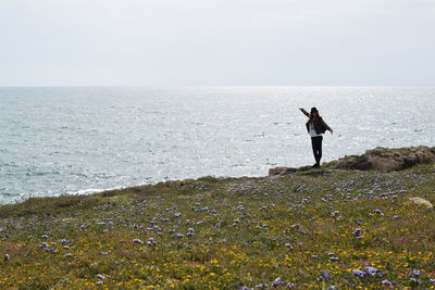 Flowers blooming against woman standing on cliff against sea