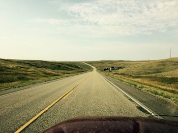 Road passing through field against sky