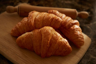 Croissants on a cutting board with a rolling pin on a table.