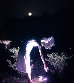 Man dancing in illuminated sea against sky at night