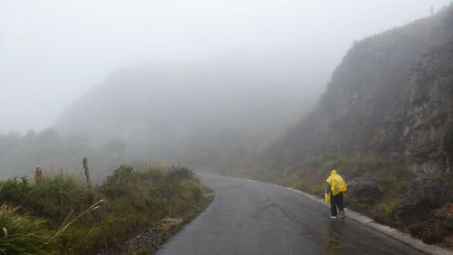 Rear view of person walking on mountain road during monsoon