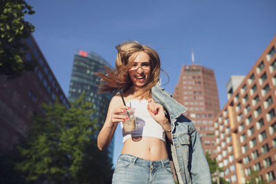 Portrait of smiling woman having coffee against buildings