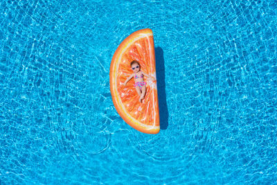 High angle view of baby girl relaxing on orange shaped pool raft