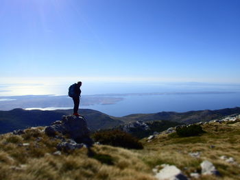 Man standing on rock looking at mountain against sky