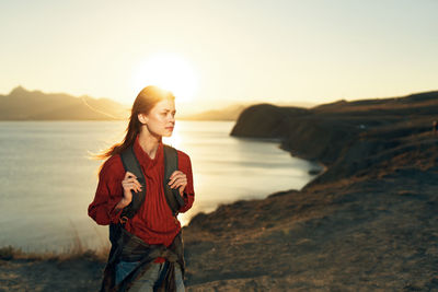 Young woman standing by sea against sky during sunset