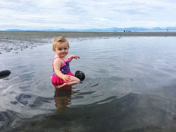 Full length side view portrait of cute baby girl sitting in sea on shore