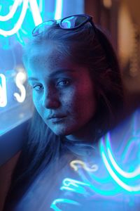 Close-up portrait of young woman sitting by illuminated window